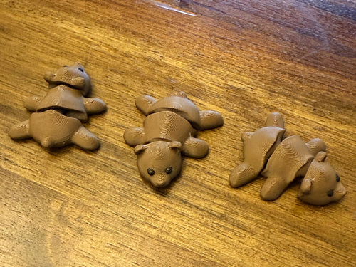 Three brown flexi bears on a wood table posed with their articulated bodies bent in different directions