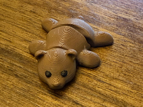 Brown 3D printed Mini Flexi Bear fidget toy with black eyes on a wood table