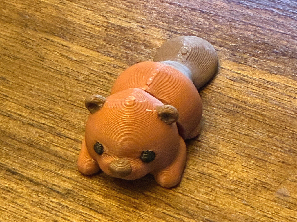 Orange-brown 3D printed Mini Flexi Beaver with a tan paddle tail, three-quarter front view on a wood table