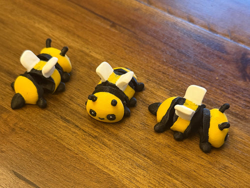 Three flexi bumblebees on a wood table with their striped abdomens curled in different poses