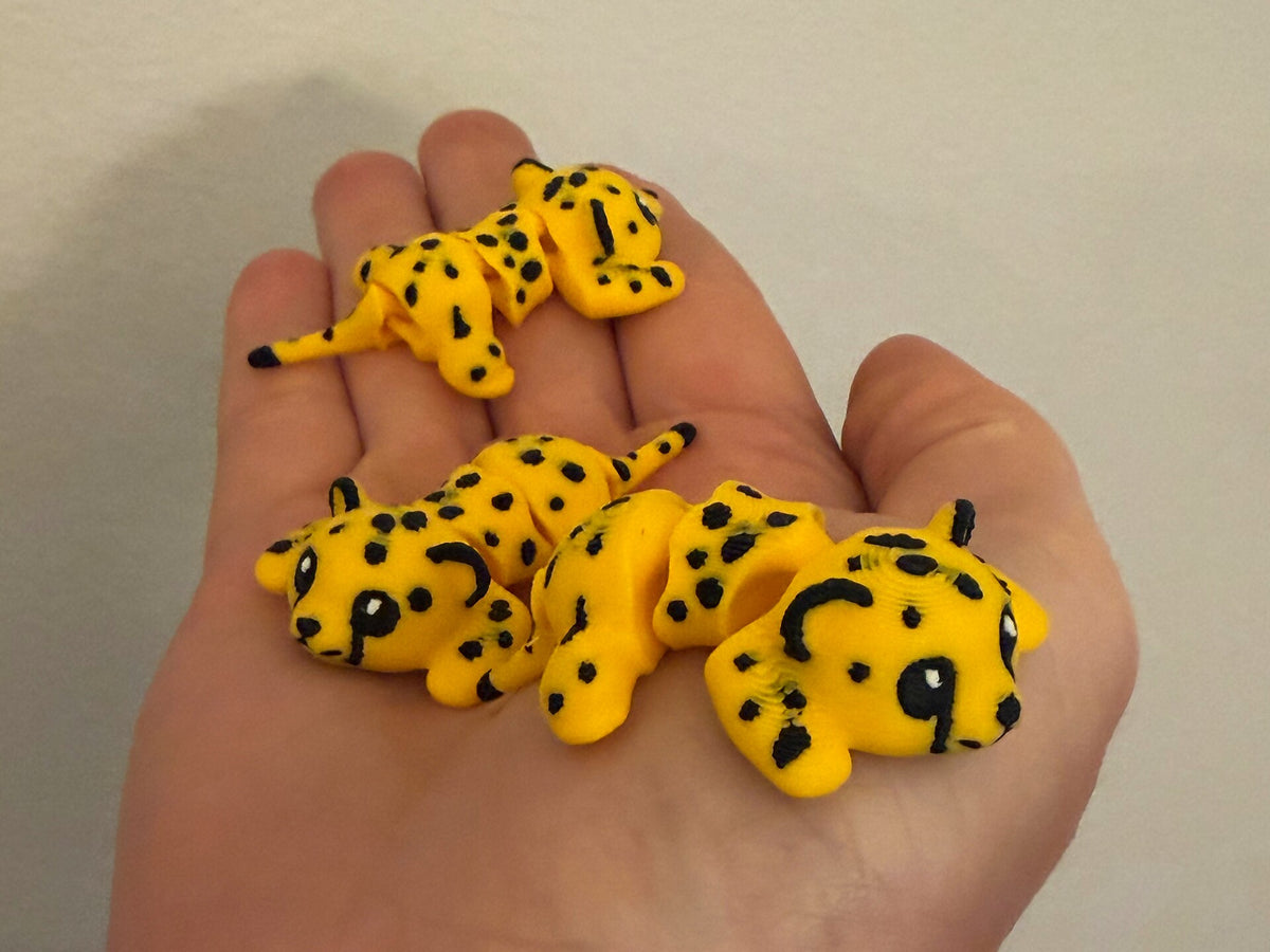 Three yellow spotted 3D printed Mini Flexi Cheetahs resting in an open hand
