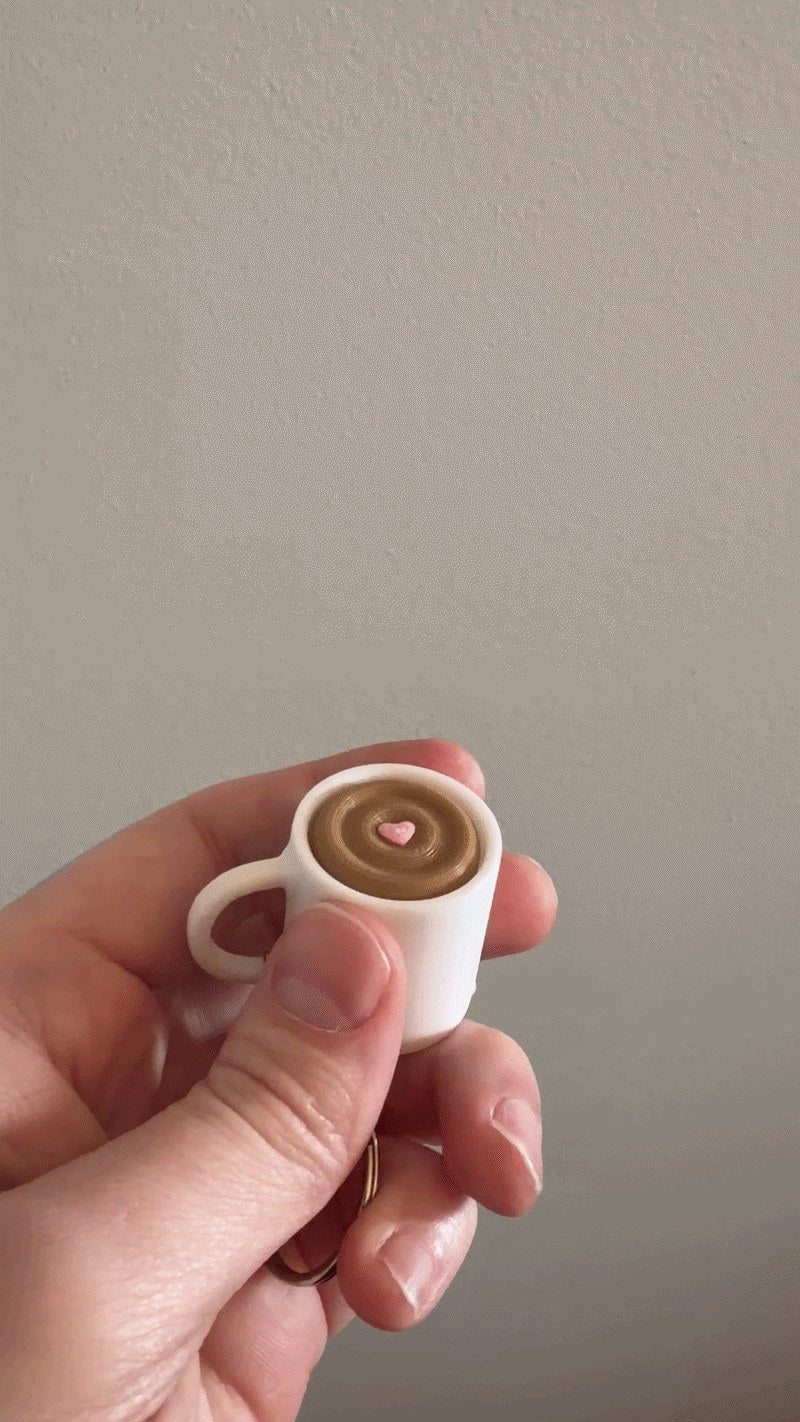 Coffee Cup Clicker Keychain held between two fingers to show its tiny size