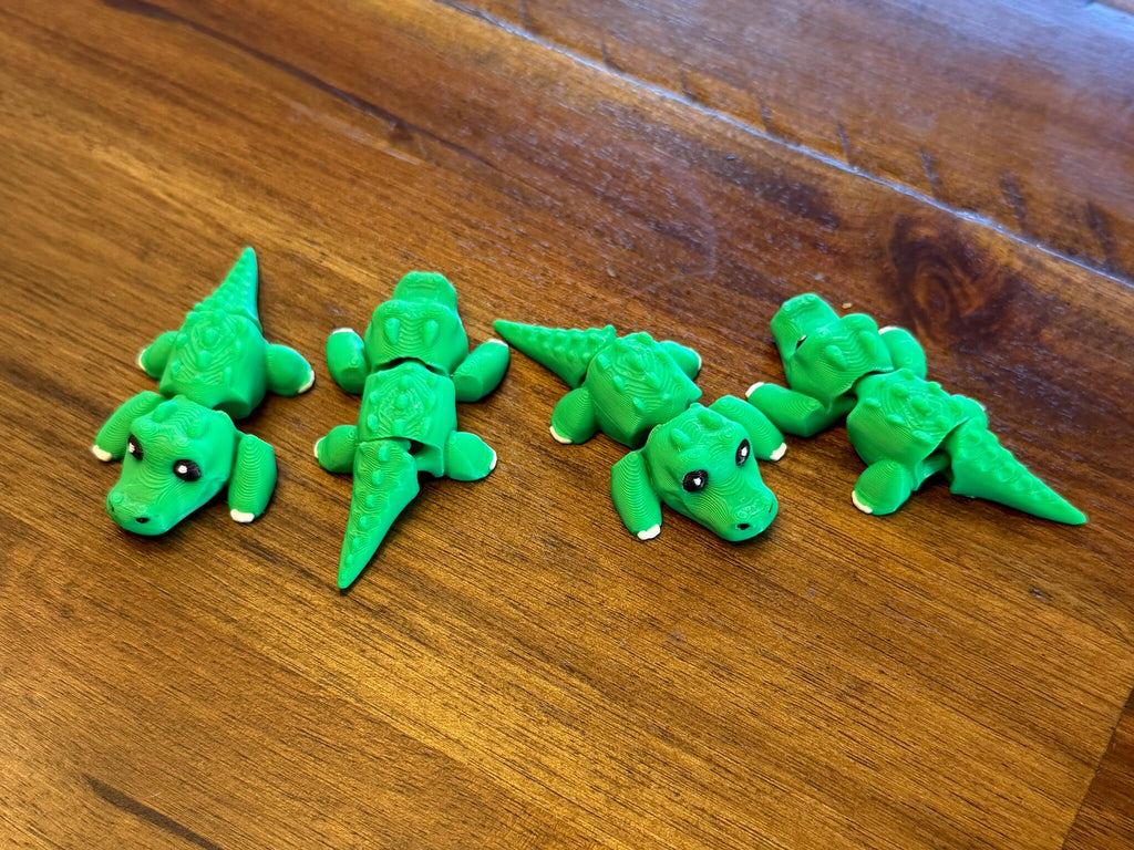 Four green 3D printed flexi alligators posed with tails bent in different directions, showing the articulated joints
