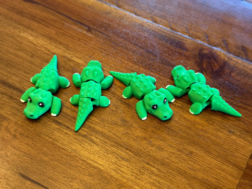 Four green 3D printed flexi alligators posed with tails bent in different directions, showing the articulated joints