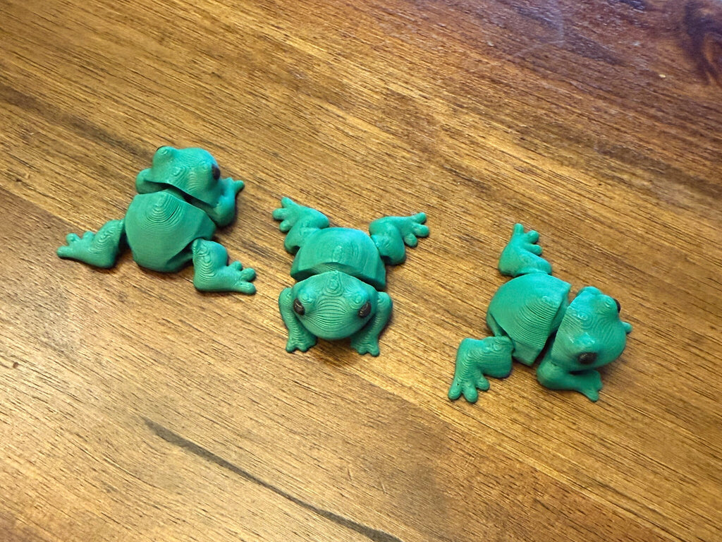Three green flexi frogs on a table shown from multiple angles