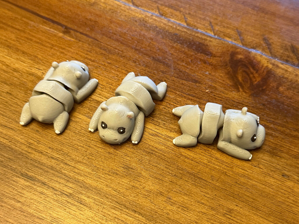 Three grey flexi hippos on a wood table posed with their articulated bodies bent in different directions