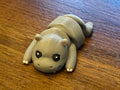Grey 3D printed Mini Flexi Hippo with pink ears, white toes, and big eyes on a wood table