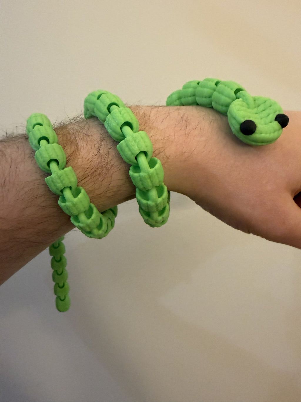 Green 3D printed Knit Articulated Snake coiled around a wrist, showing its flexible knit-textured segments