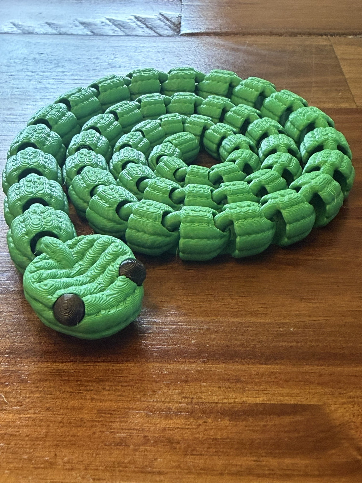 Large Knit Articulated Snake in green, coiled in a tight spiral on a wood table
