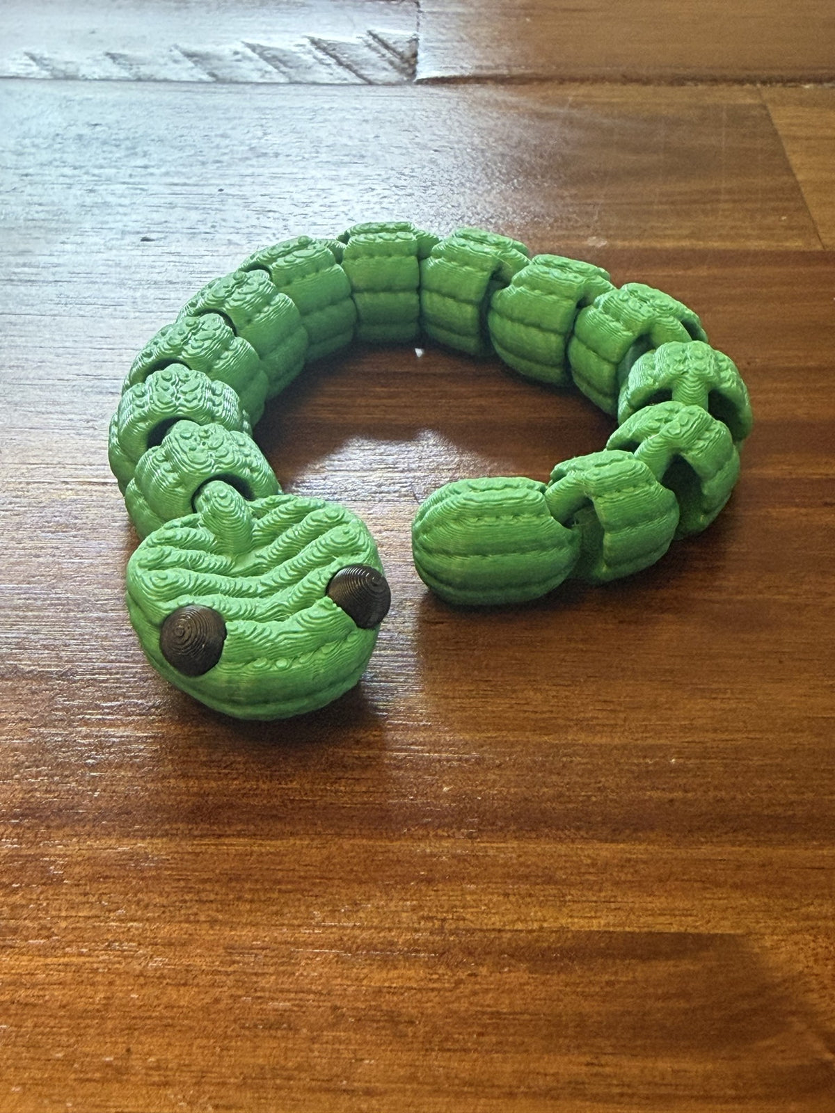 Medium Knit Articulated Snake in green, curled in a loop on a wood table