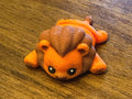 Orange 3D printed Mini Flexi Lion with a brown swirled mane, three-quarter front view on a wood table