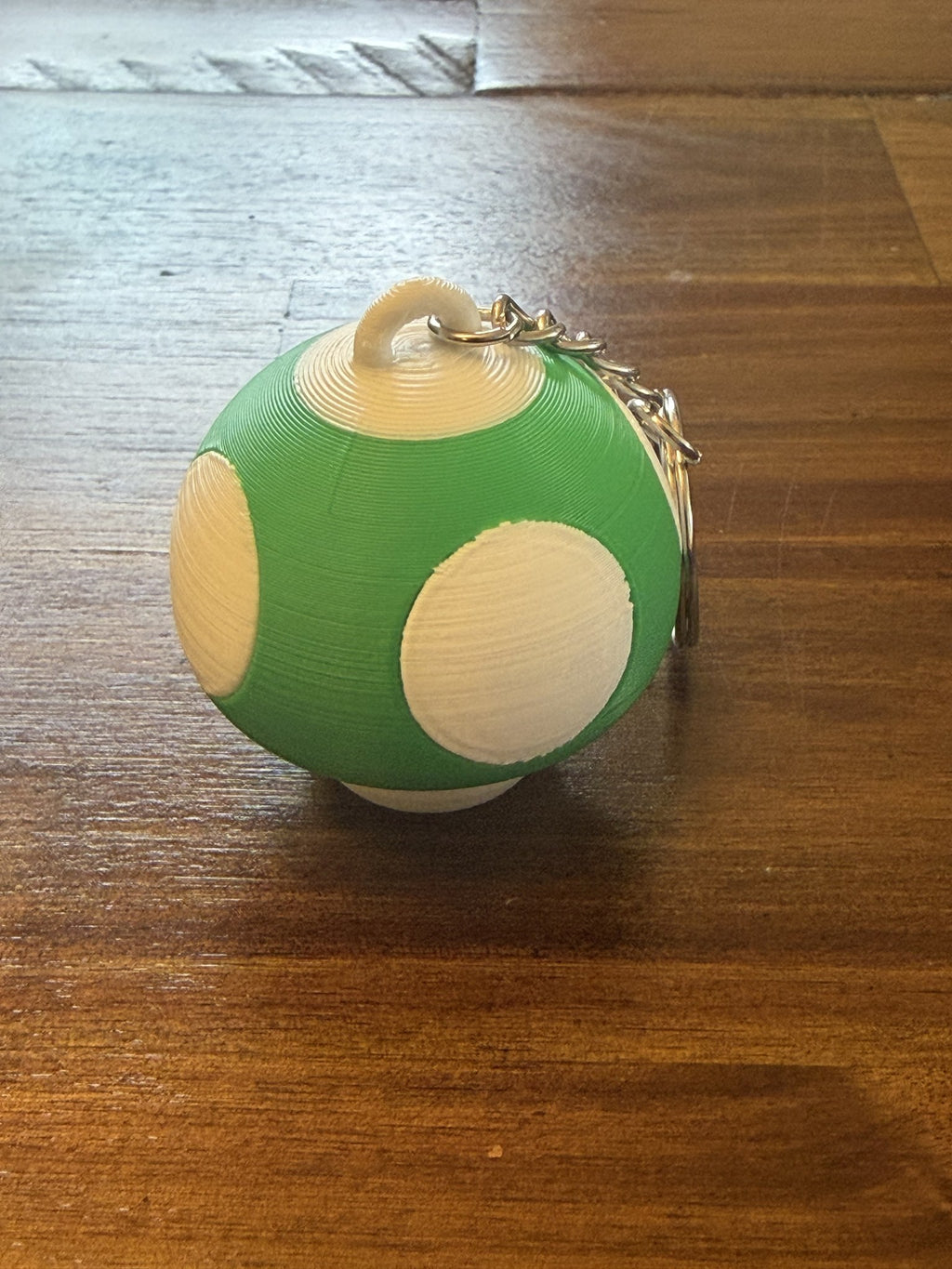Green Mushroom Clicker Keychain with cream spots on a wood table