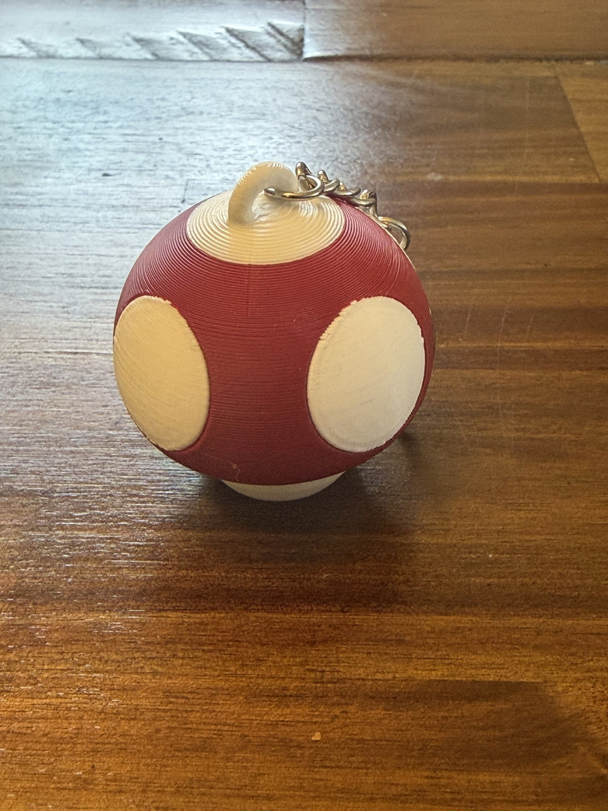 Red Mushroom Clicker Keychain with cream spots on a wood table