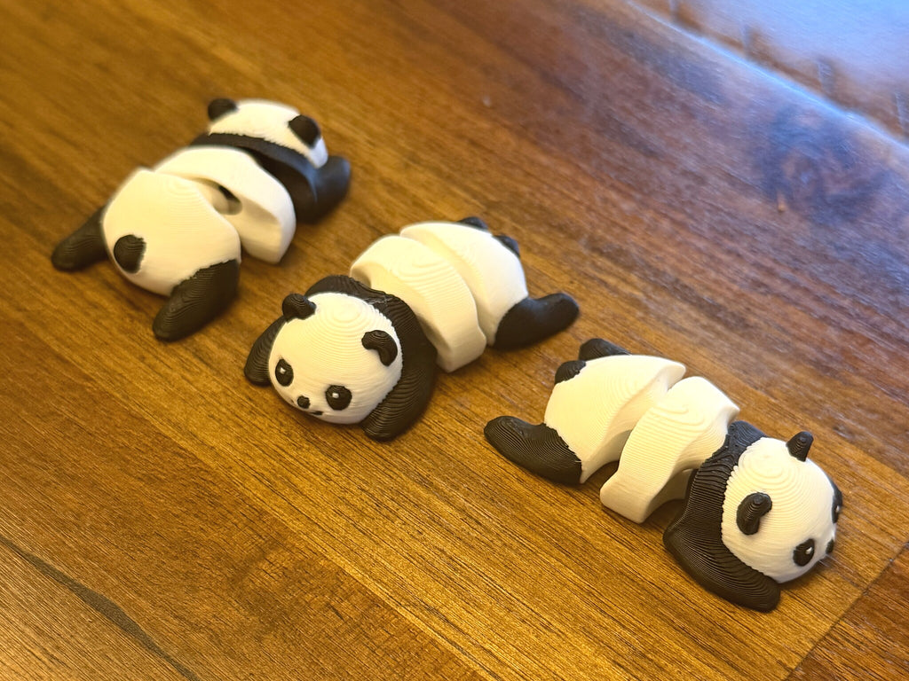 Three flexi pandas lined up on a wood table