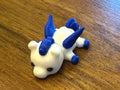 White 3D printed Mini Pegasus figurine with blue wings, mane, and tail, three-quarter view on a wood table