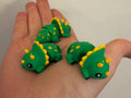 Three green 3D printed Mini Flexi Triceratops with yellow spikes resting in an open palm